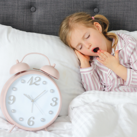 Enfant au lit qui bâille près d’un réveille-matin